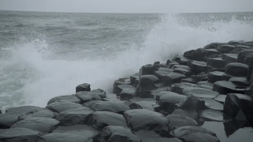 The waves crash against the rocks of the shore