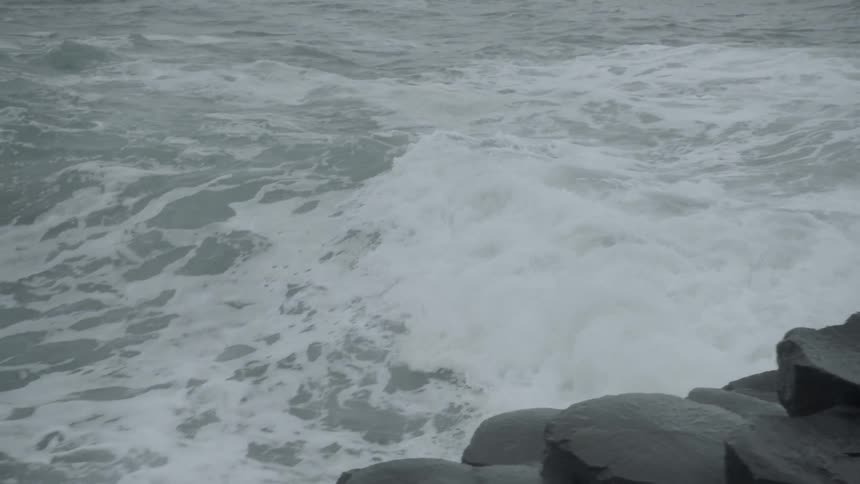 Ocean waves crash into a rocky shoreline on an overcast day