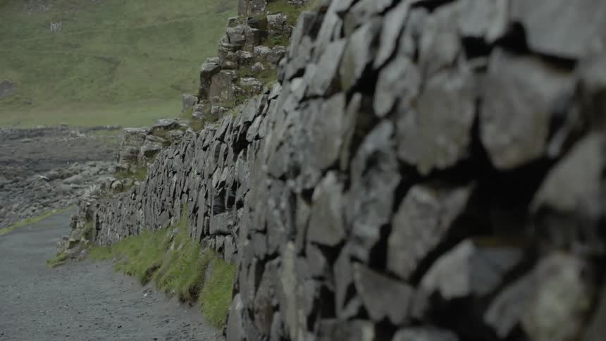 A wall built out of dark stones lines the side of a path