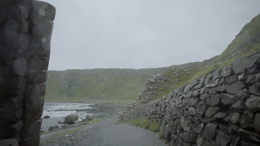 A path winds done past a stone wall to the shore of a bay
