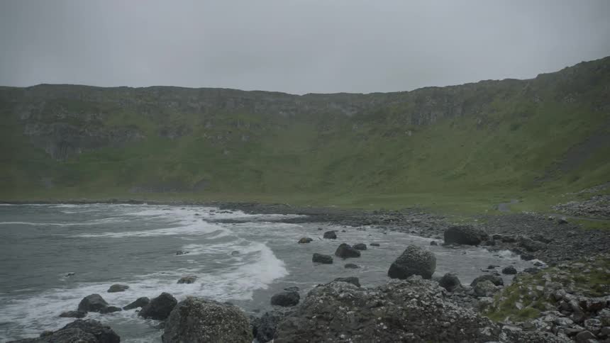 A mountain range with grass on the hills that roll down to the ocean