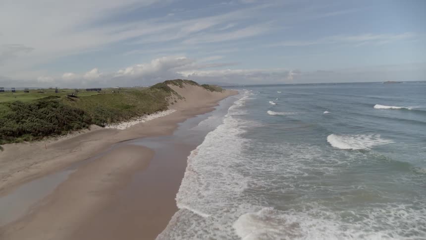 Waves lap on a sandy beach next to a golf course