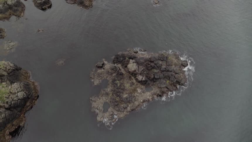 An aerial view of water flowing against rocks in the ocean