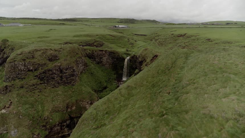 A green cliff with a waterfall with the sky in the background
