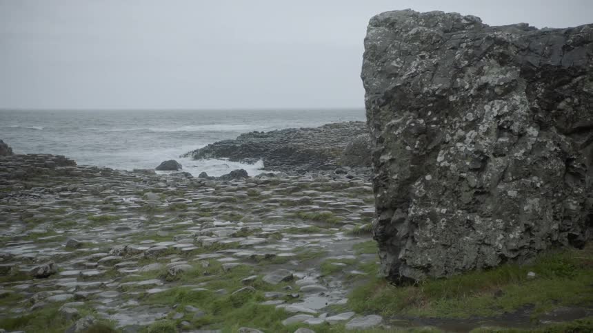 Large boulders sit on a rocky shore as ocean waves splash and break