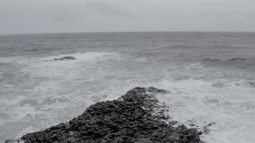 Ocean waves crash and splash over a rocky shore on a gray day
