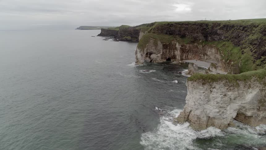 The waves crash against the cliffs on the shore on a cloudy day
