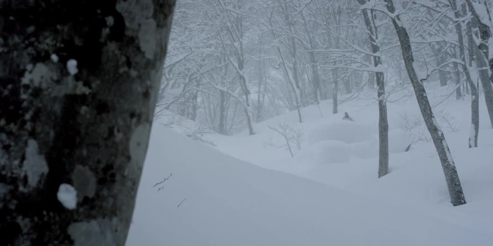 Snow falls as a skier rides down through deep powder