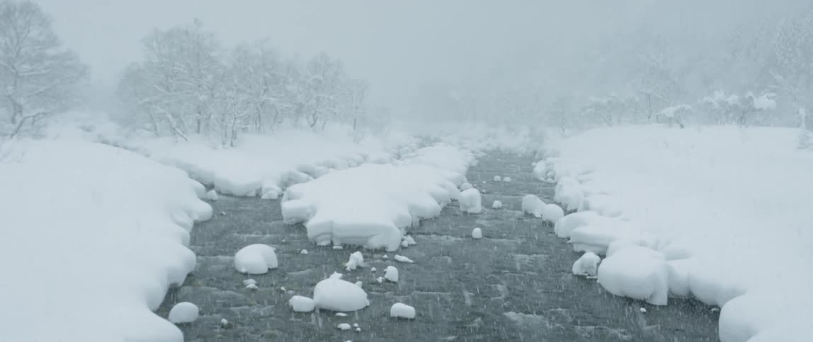 A rushing river covered in snow near a field and trees