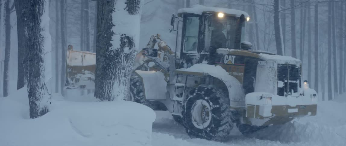 A bulldozer clearing snow next to trees