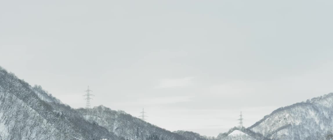 Power towers stand on tree covered snowy hills and ridges