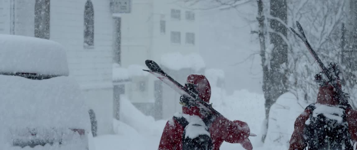 A group of people walk down the street with skis in the snow