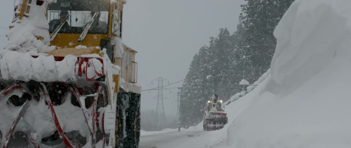 Snow ploughs attempt to clear a road under heavy snowfall in poor visibility