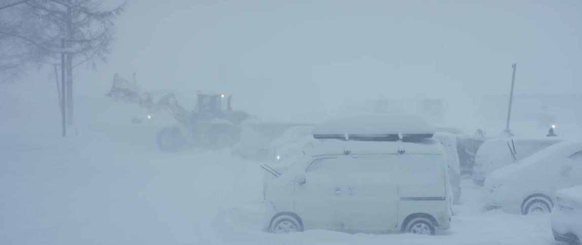 A bulldozer clears snow in a parking lot during a snow storm