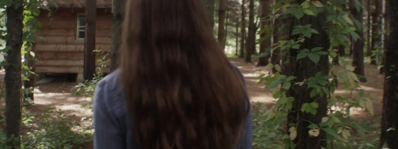 Woman walks toward a cabin in the woods