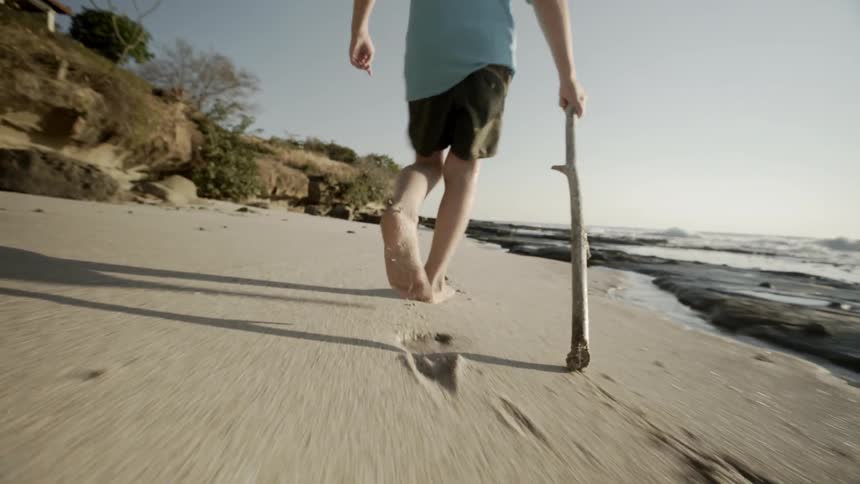 Child drags stick along sand at beach