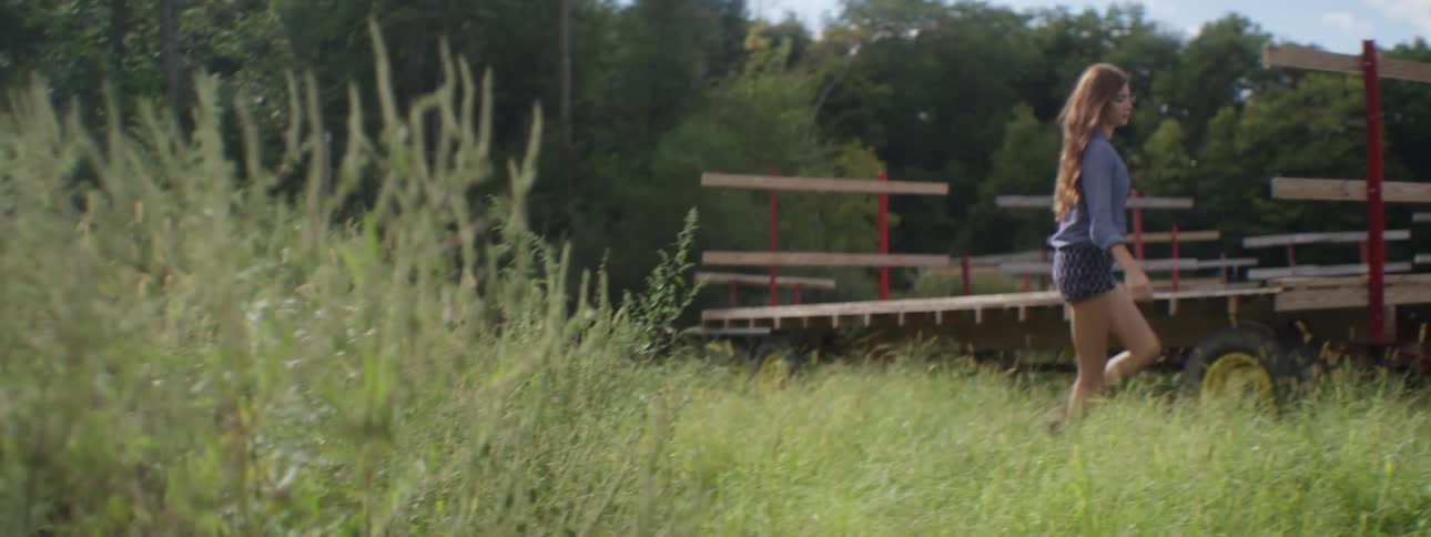 A woman walks through tall grass in a wooded area