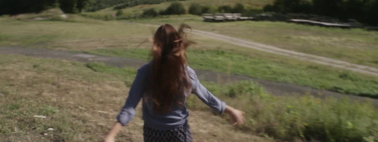 A woman runs on grass toward a small road