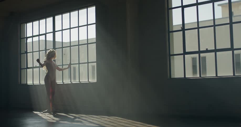 Woman practices ballet as she stands near a window