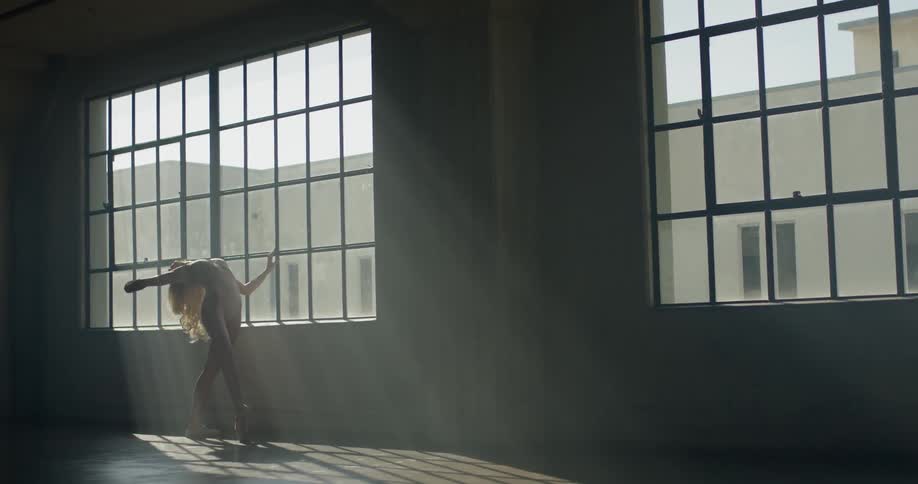 A young white woman practices ballet moves in a dance studio
