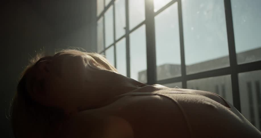 A woman leans back and stretches her arms behind her by a window