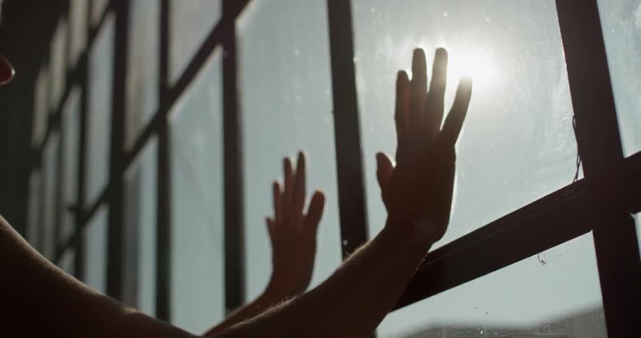 Woman places her palms on adjoining glass panes in a large window