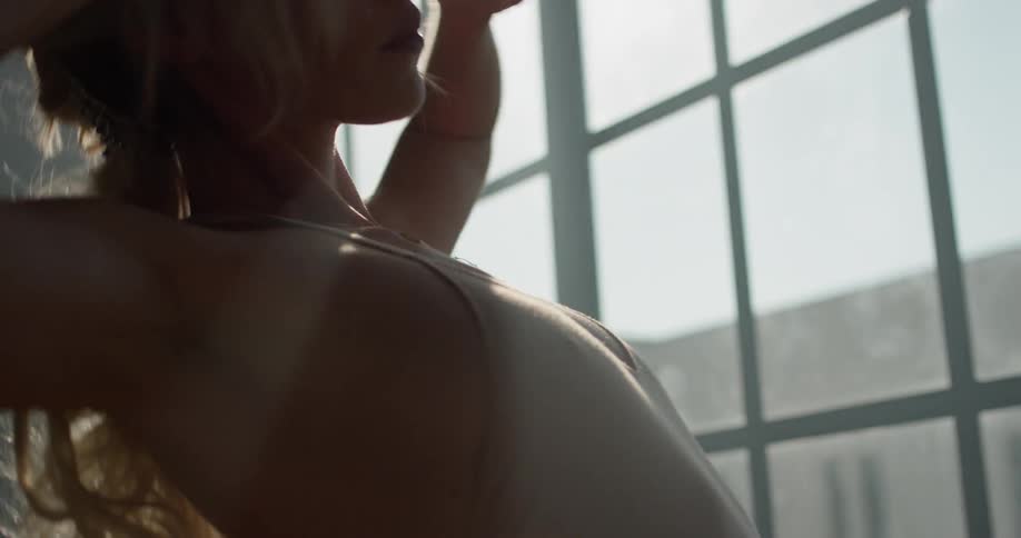 A young woman dances in a dance studio while standing in front of a large window