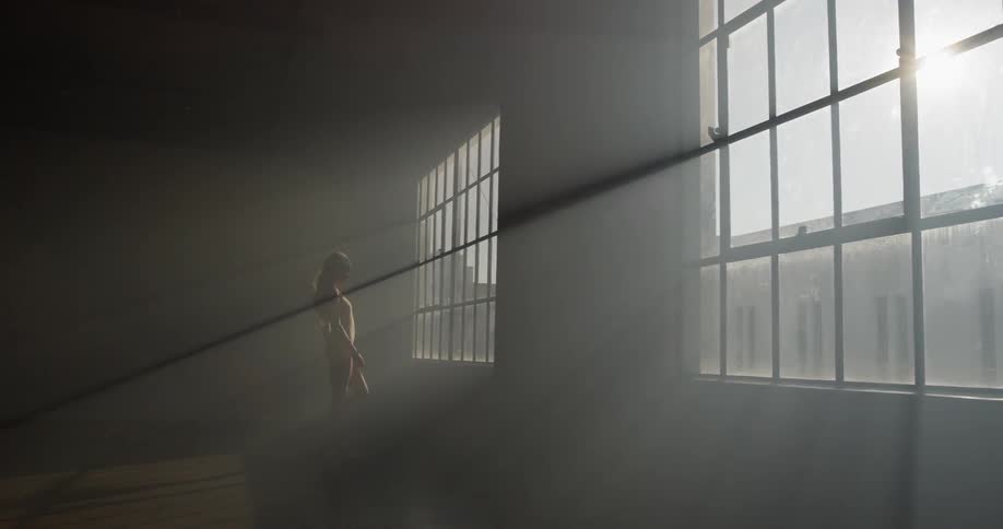 A ballerina walks towards a sunny window in a dance studio