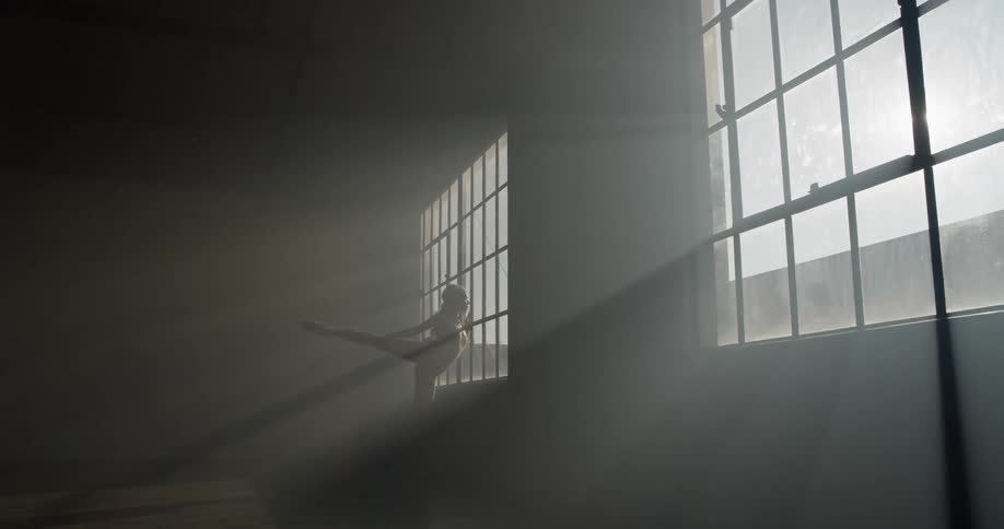 A ballerina stretches in front of a sunny window in a dance studio