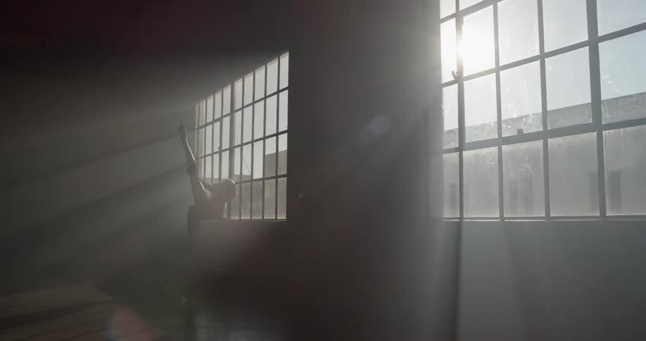A woman in a dance studio stretching her legs near a window