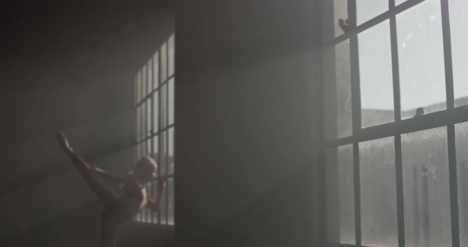 A woman walks to a window and stretches her leg up and out