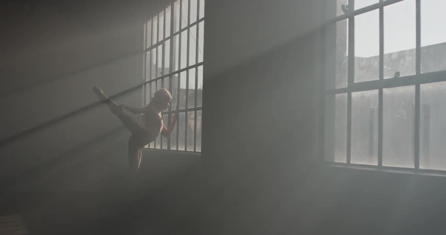 A woman in a bodysuit walks to a georgian window and performs a stretch