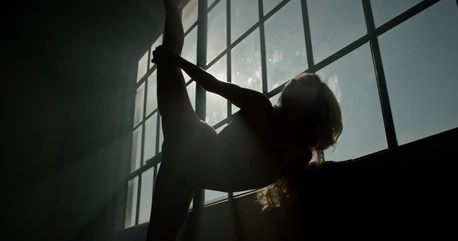 The silhouette of a dancer stretching in front of a large window with sun shining through