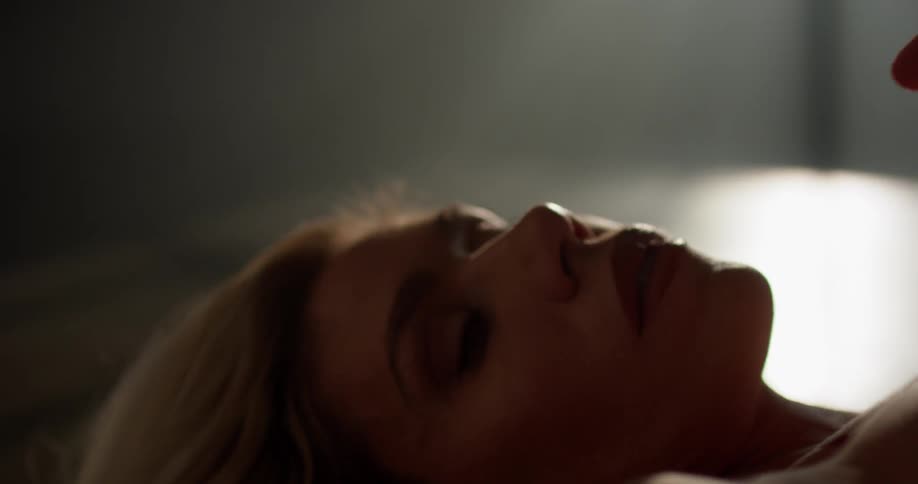 A woman sensually rubs her hands down her chest while lying down in a room