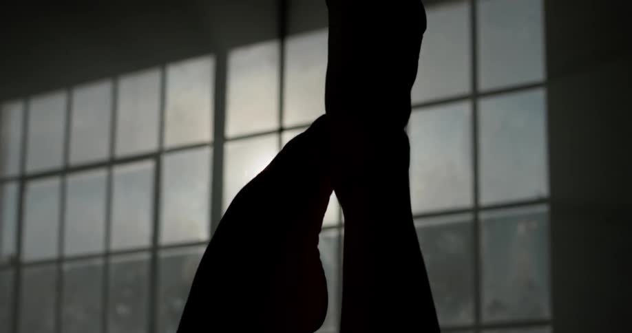 A pair of shadowy feet making graceful motions in from of window in a dimly lit room
