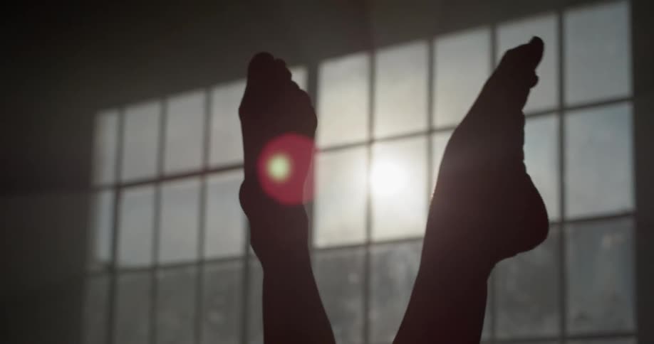 Silhouette of ballerinas feet dance in front of window while the sun shines