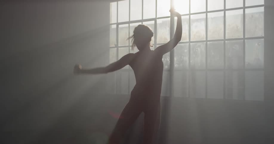 A female dancer twirls and jumps in front of a sunny window in a dance studio