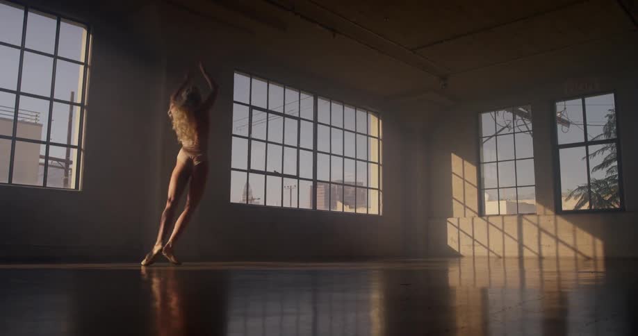 A ballerina in a pink leotard pirouettes and rehearses in a dance studio