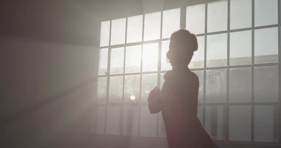 A woman in a bodysuit performs dance moves in front of a georgian window letting in the sunlight