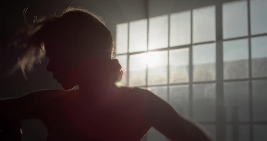A woman dances in a dance studio lit only by the morning sun