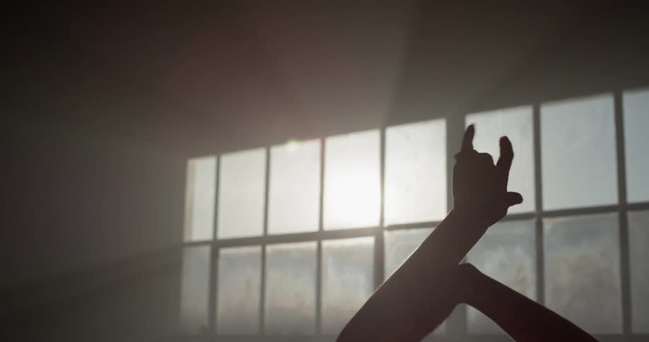 A woman moves her hands in a rhythmic motion in front of a large window