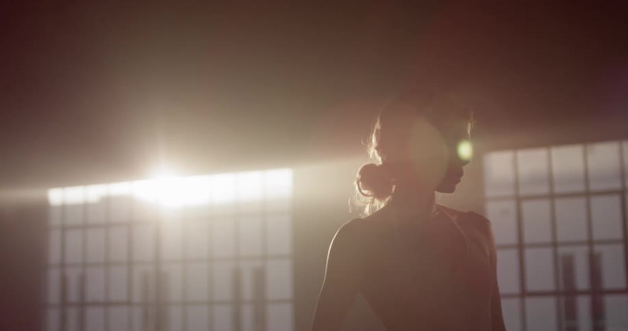 A woman in a dance studio standing with windows and the sun in the background