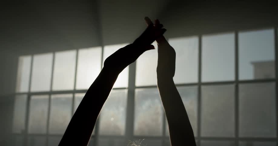 Silhouette of ballerinas arms dance in front of window indoors while the sun shines