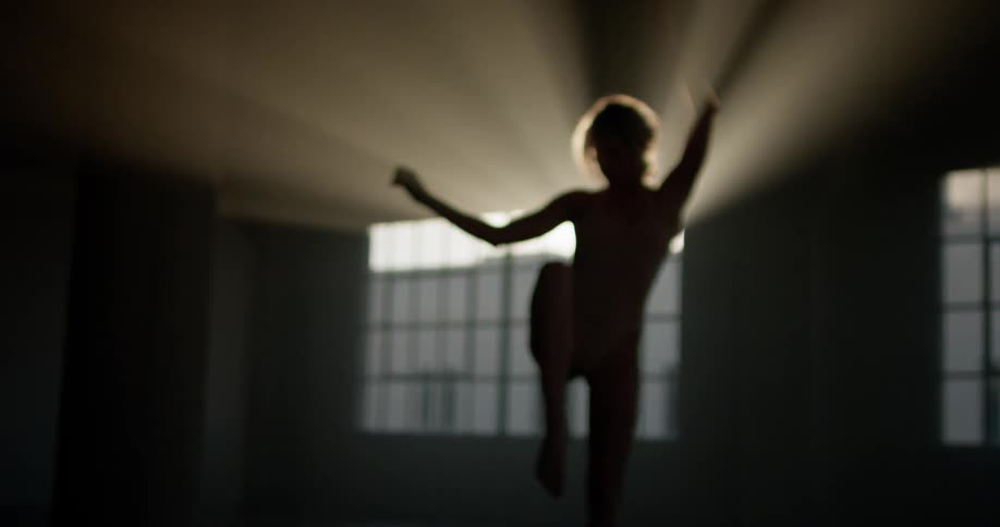 A woman dances in a dark room as sunlight shines through a window