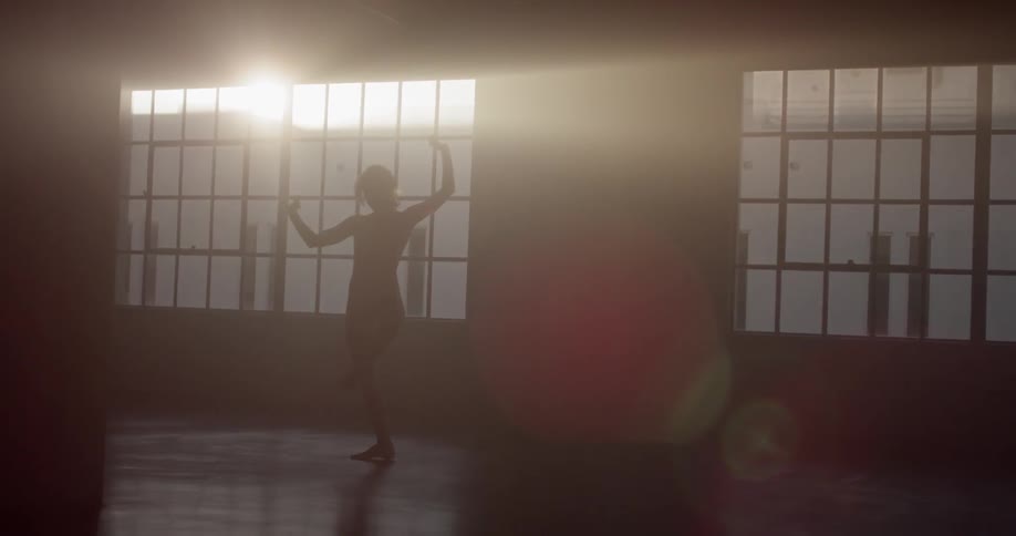 A ballerina dances in front of a sunny window in a dance studio