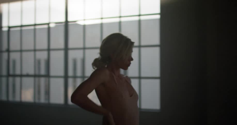 A ballerina in a pink leotard dances in front of a window in a dance studio