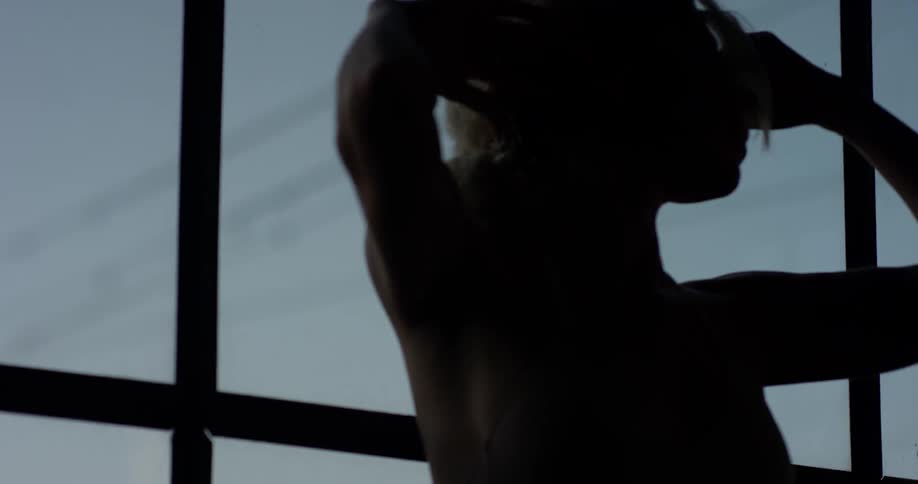 Power lines are shown outside a window as the camera adjust focus to show a woman stretching her arms