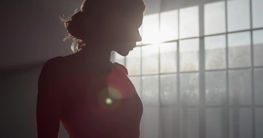 A white woman in a leotard stands in a large room