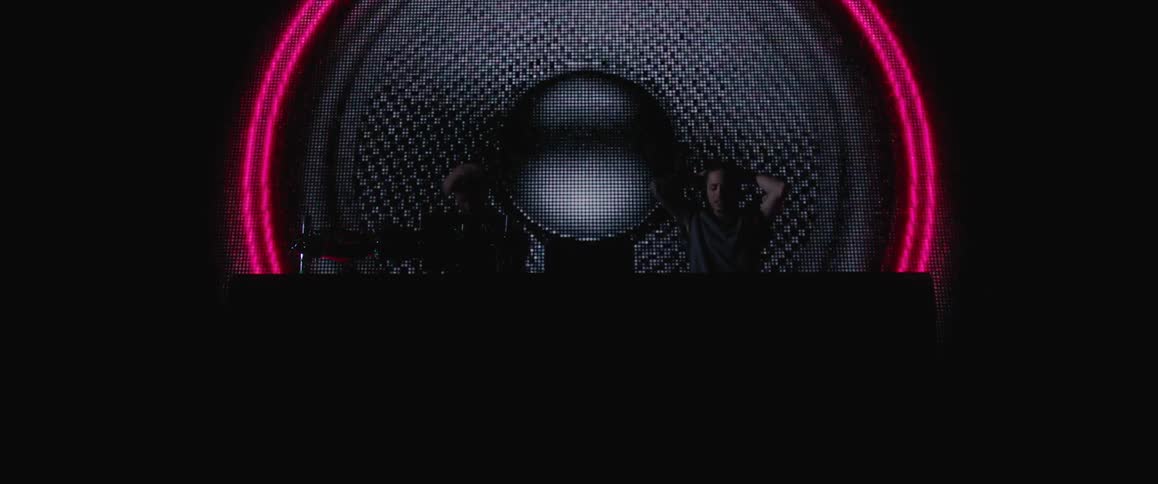 Two DJs performing in a dark room with large pulsating graphics displayed behind them
