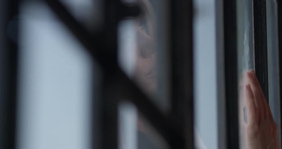 Woman near a window watching her own reflection staring back at her